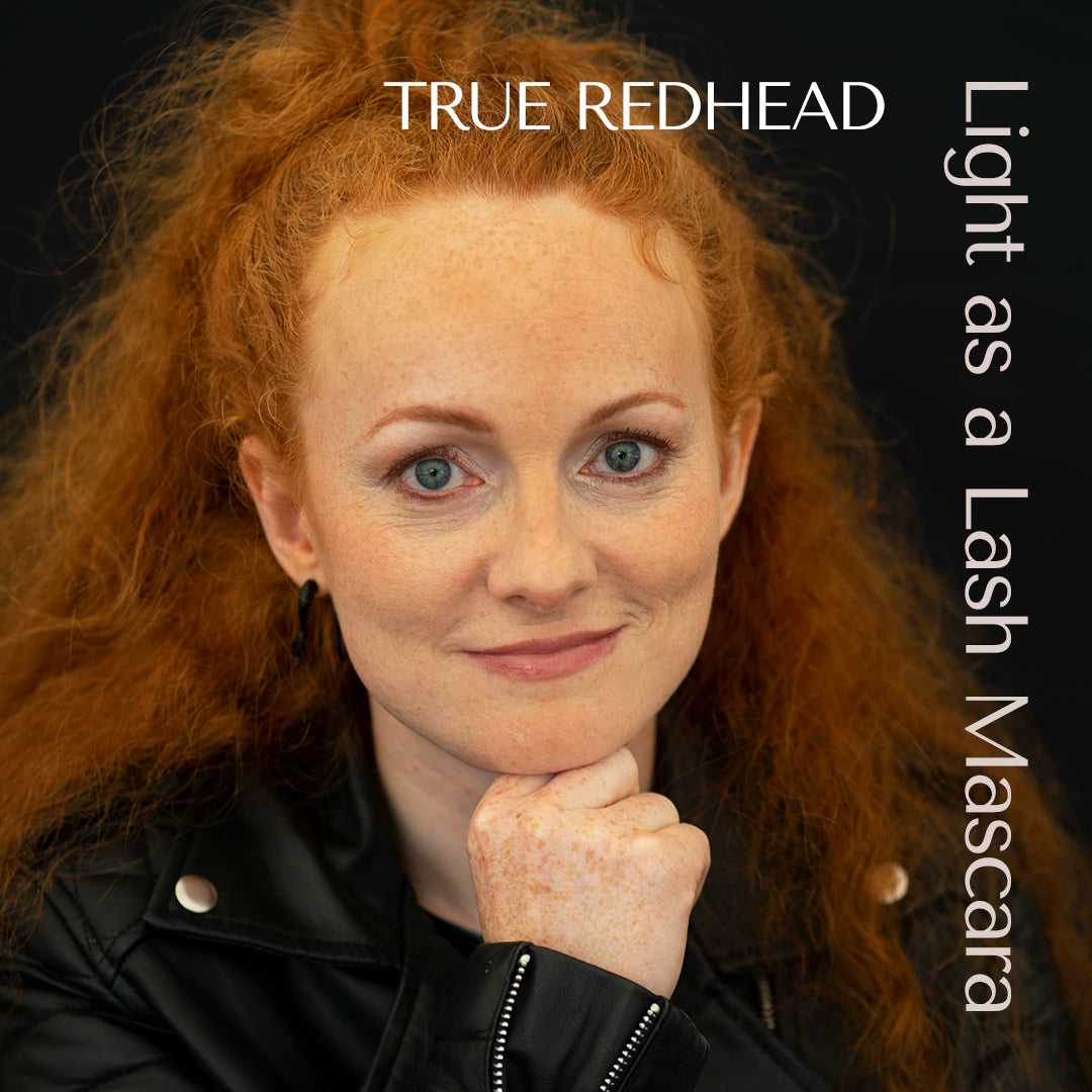 Redhead with very big curly hair and leather jacket wears delicate make up by hey redhead. Mascara and brow mascara for redheads and gingers. Calling all gingers. Calling all redheads. She wears the shade true redhead mascara. 