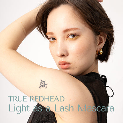 beautiful asian and nordic model with short balck hair and fair skin with tatoo wears True Redhead mascara from the line light as a lash mascara from HEY REDHEAD. Warm tones shade of brown mascara. Earthy brown, red earth mascara.  